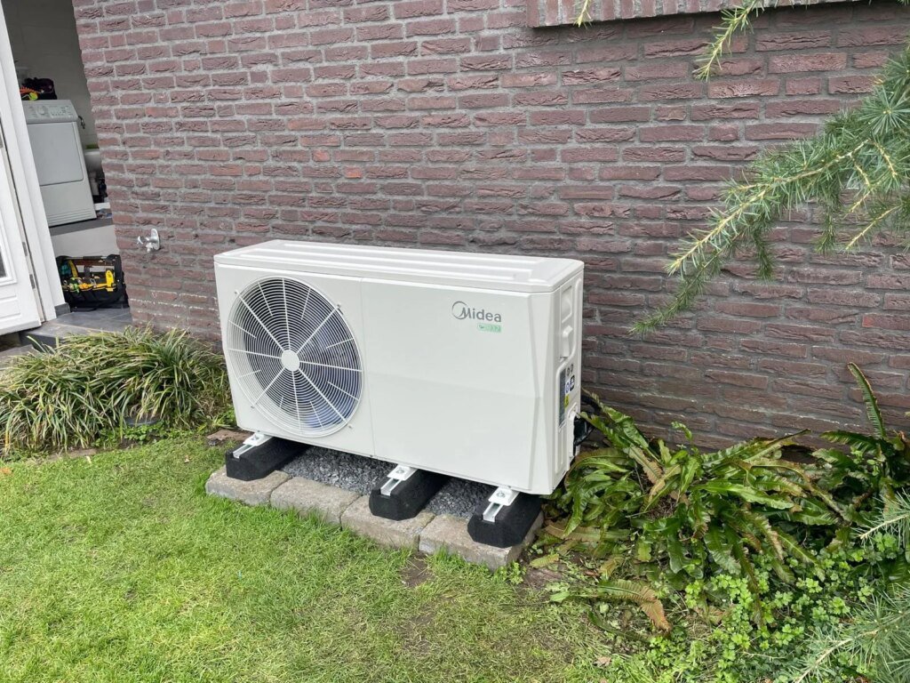 Midea warmtepomp buitenunit opgesteld in tuin tegen gevel